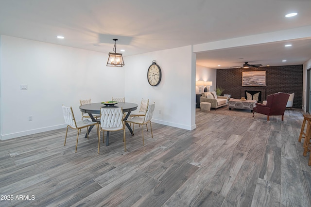 dining area featuring ceiling fan, hardwood / wood-style flooring, brick wall, and a brick fireplace