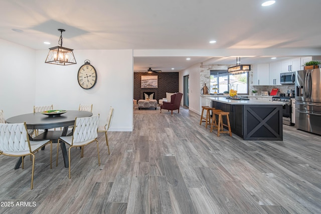 dining area with a brick fireplace, light hardwood / wood-style floors, and ceiling fan