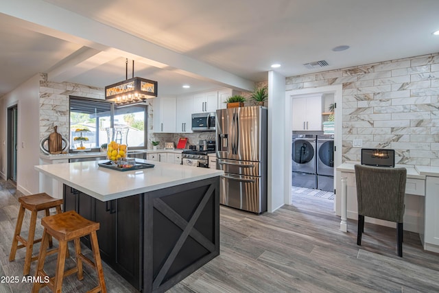 kitchen featuring appliances with stainless steel finishes, tasteful backsplash, white cabinets, decorative light fixtures, and washer and dryer