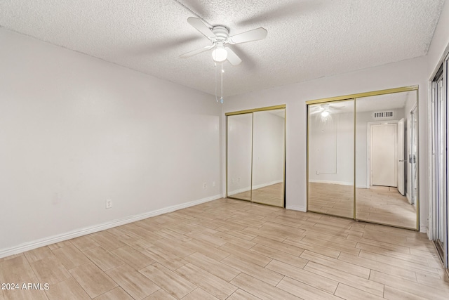 unfurnished bedroom featuring ceiling fan, a textured ceiling, two closets, and light hardwood / wood-style floors