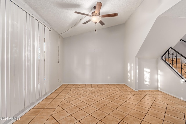 tiled spare room featuring lofted ceiling, ceiling fan, and a textured ceiling