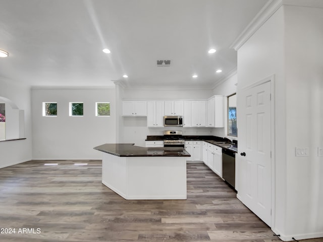 kitchen featuring appliances with stainless steel finishes, crown molding, wood-type flooring, white cabinets, and a center island