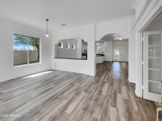 unfurnished living room with plenty of natural light, hardwood / wood-style floors, crown molding, and french doors