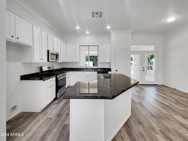 kitchen with white cabinets, light wood-type flooring, ornamental molding, appliances with stainless steel finishes, and a kitchen island