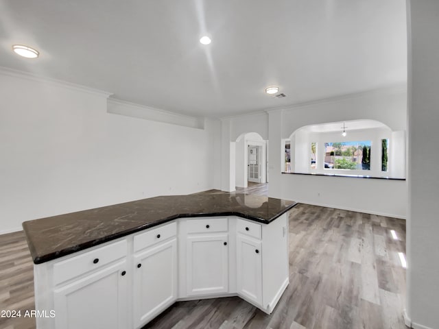 kitchen featuring white cabinets, light hardwood / wood-style flooring, crown molding, and dark stone countertops