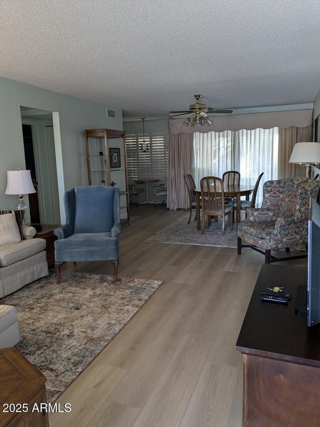 living room featuring a textured ceiling, ceiling fan, and light wood-style flooring