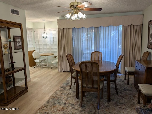 dining room featuring a textured ceiling, ceiling fan with notable chandelier, wood finished floors, and visible vents