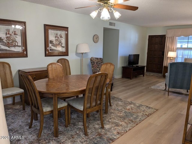 dining area with light wood-type flooring, visible vents, ceiling fan, and a textured ceiling