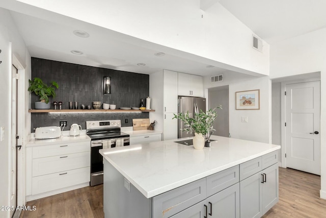 kitchen featuring wood-type flooring, appliances with stainless steel finishes, a center island, and gray cabinetry