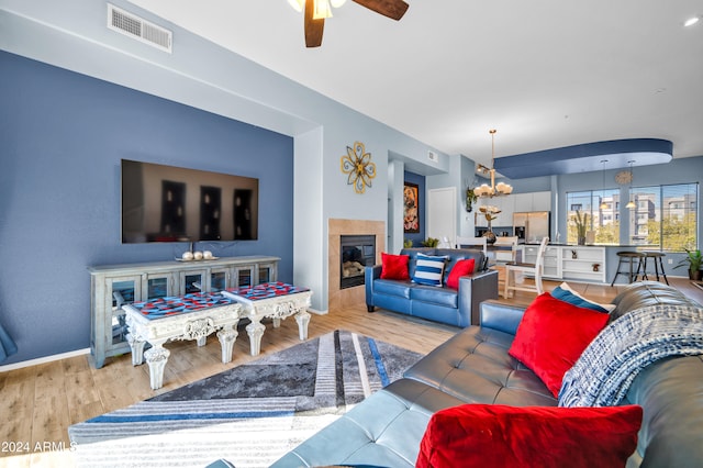 living room with light hardwood / wood-style flooring, a tile fireplace, and ceiling fan with notable chandelier