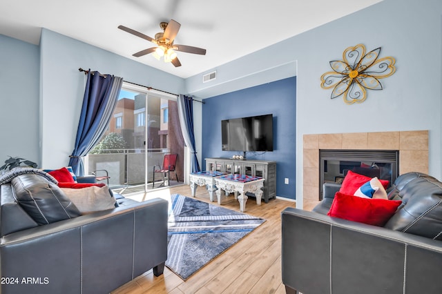 living room featuring hardwood / wood-style flooring, a tiled fireplace, and ceiling fan