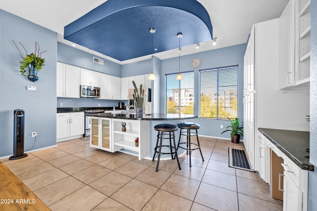 kitchen featuring white cabinets, a center island with sink, light tile patterned floors, appliances with stainless steel finishes, and decorative light fixtures