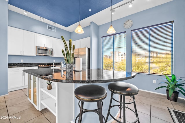 kitchen with appliances with stainless steel finishes, an island with sink, white cabinetry, pendant lighting, and light tile patterned floors