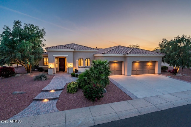 mediterranean / spanish house with a garage, stucco siding, concrete driveway, and a tiled roof