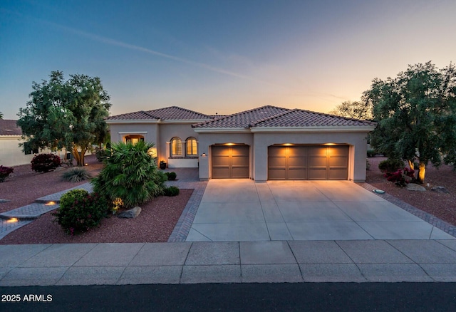 mediterranean / spanish-style house featuring a garage, stucco siding, a tiled roof, and concrete driveway