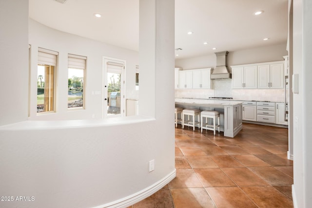 kitchen featuring a breakfast bar area, backsplash, light countertops, custom exhaust hood, and white cabinetry
