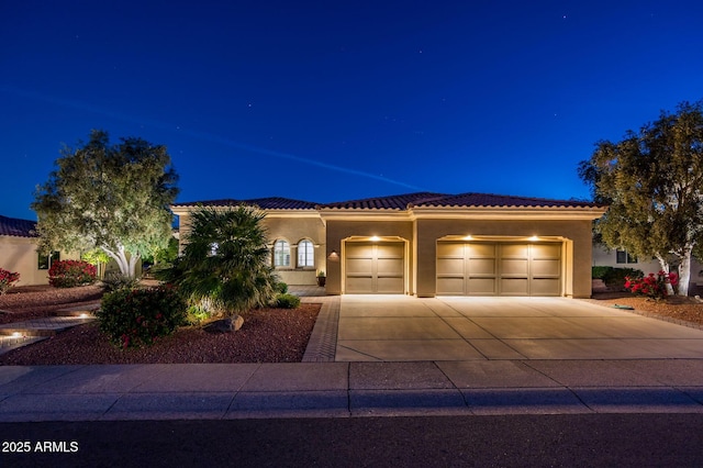 mediterranean / spanish home with an attached garage, concrete driveway, a tile roof, and stucco siding