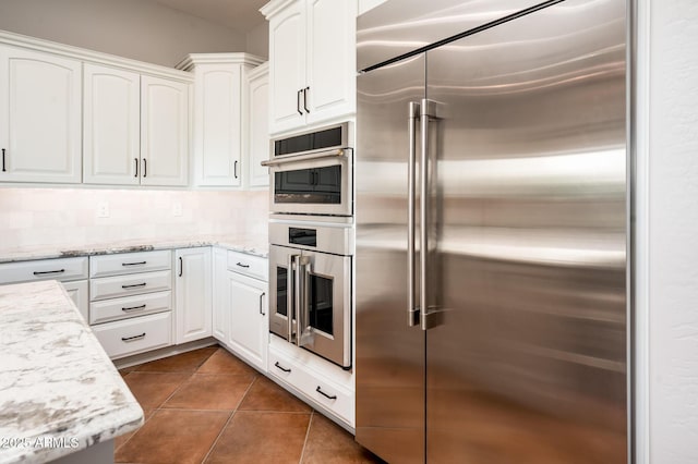 kitchen featuring appliances with stainless steel finishes, white cabinets, light stone countertops, and dark tile patterned floors