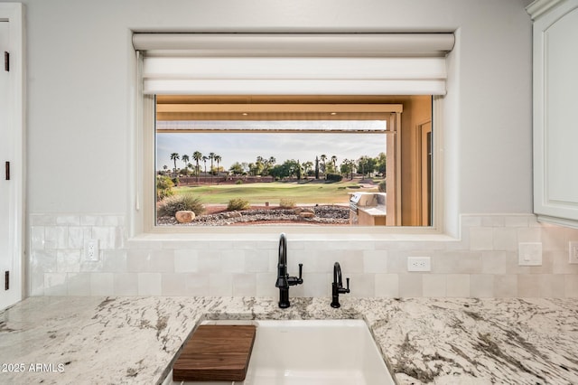 interior details with light stone counters, a sink, white cabinetry, and backsplash