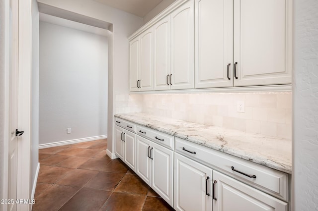 kitchen featuring baseboards, white cabinetry, light stone counters, and tasteful backsplash