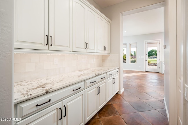 kitchen featuring light stone countertops, white cabinetry, baseboards, decorative backsplash, and dark tile patterned floors