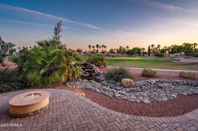 yard at dusk featuring a patio, a fire pit, and golf course view