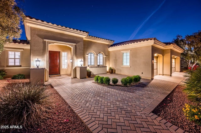 back of house at twilight with stucco siding and a tiled roof