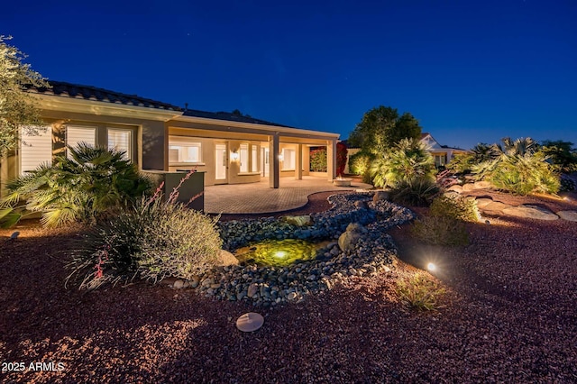 back of house at twilight featuring stucco siding, a patio area, and a tile roof