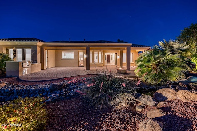 back of house at twilight featuring a patio, exterior kitchen, and stucco siding