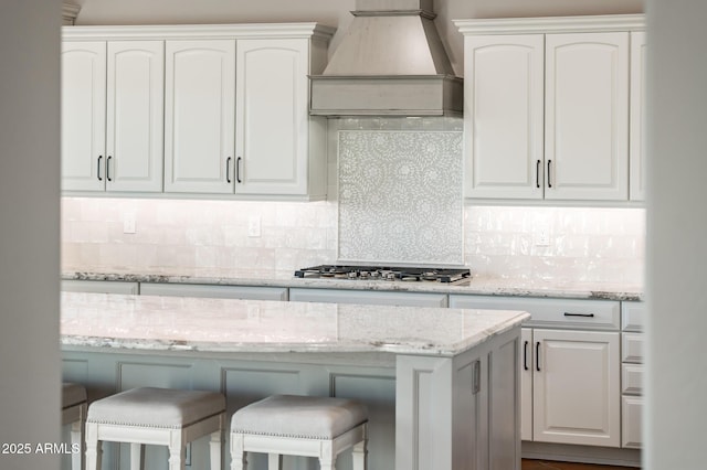 kitchen with backsplash, a breakfast bar area, custom exhaust hood, and white cabinets