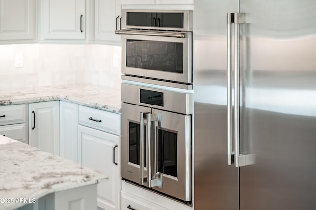 kitchen with appliances with stainless steel finishes, tasteful backsplash, light stone countertops, and white cabinetry