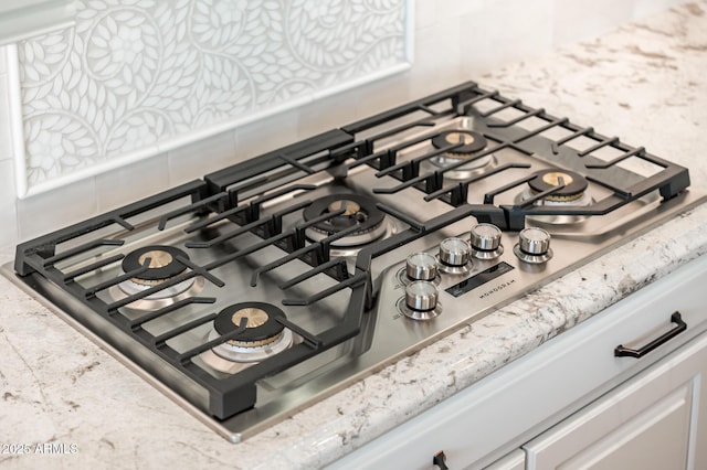 details featuring light stone counters, stainless steel gas cooktop, and backsplash