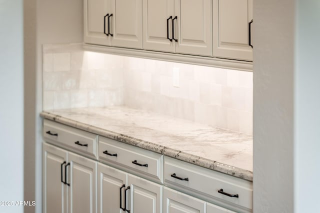 kitchen featuring backsplash, white cabinetry, and light stone countertops