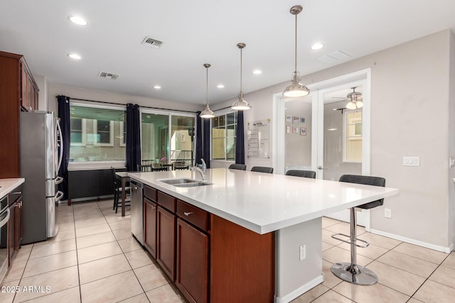 kitchen featuring an island with sink, ceiling fan, appliances with stainless steel finishes, a kitchen breakfast bar, and sink