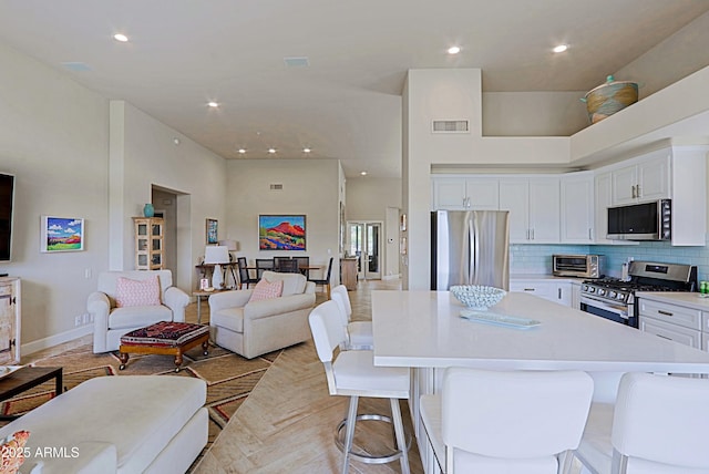 kitchen featuring white cabinets, appliances with stainless steel finishes, a breakfast bar, open floor plan, and a towering ceiling