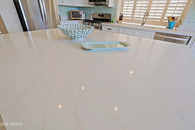 kitchen with a sink, decorative backsplash, stainless steel appliances, and white cabinetry
