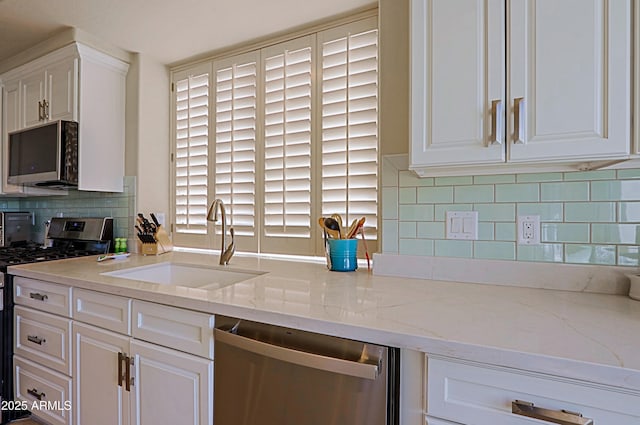 kitchen with white cabinetry, tasteful backsplash, light stone counters, a sink, and stainless steel appliances