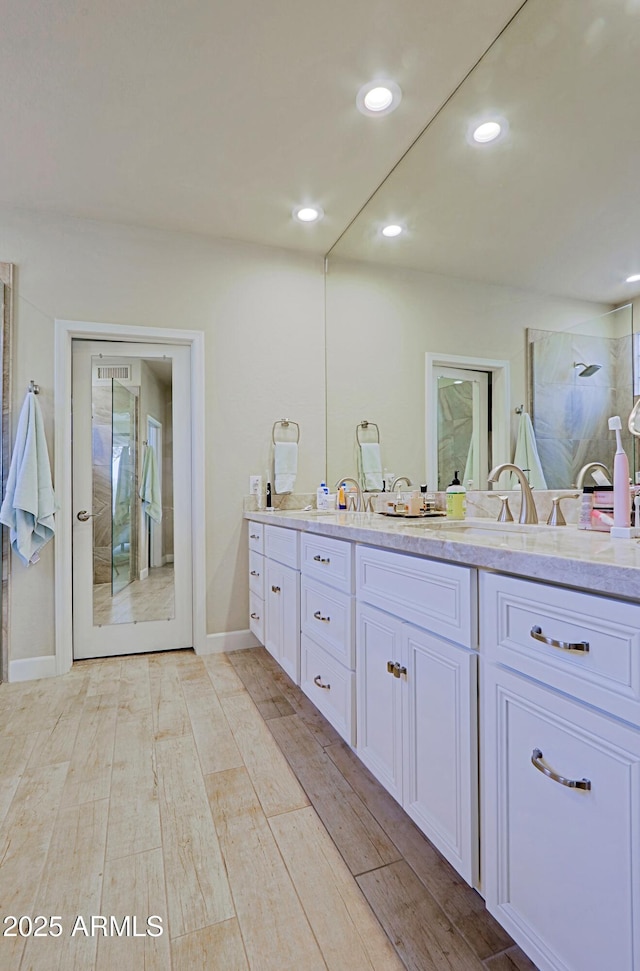 bathroom with double vanity, a tile shower, wood finished floors, baseboards, and recessed lighting