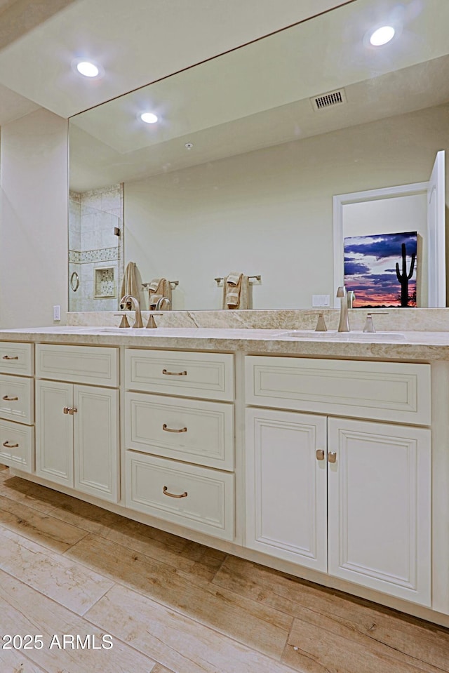 full bathroom featuring double vanity, visible vents, wood finished floors, a sink, and tiled shower