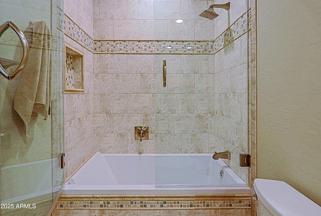 full bathroom with toilet, tiled shower / bath, and a textured wall