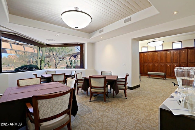 dining room with a tray ceiling, visible vents, light carpet, and baseboards