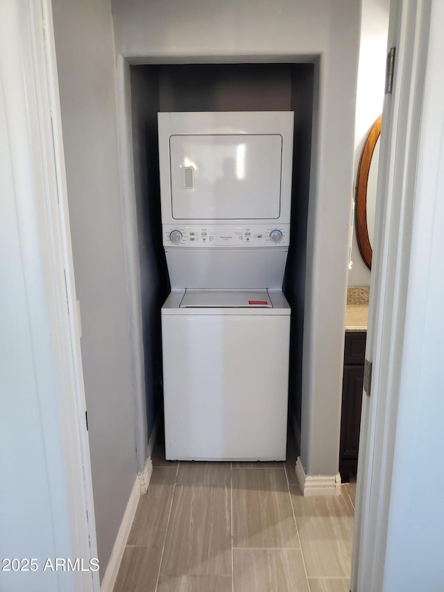 washroom with stacked washer and dryer, laundry area, and baseboards