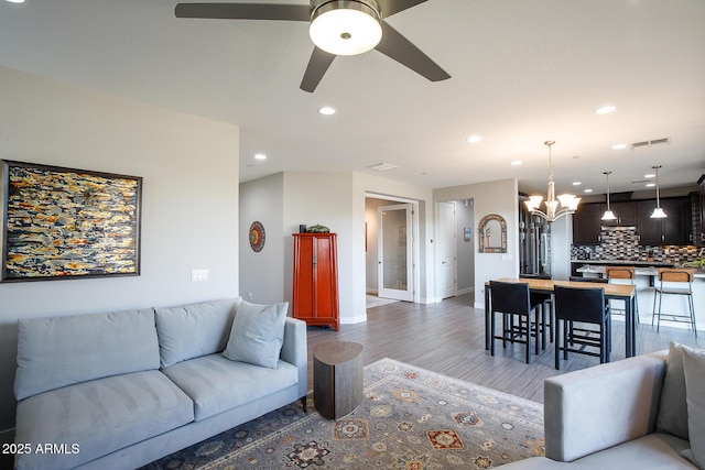 living room with ceiling fan with notable chandelier and hardwood / wood-style floors