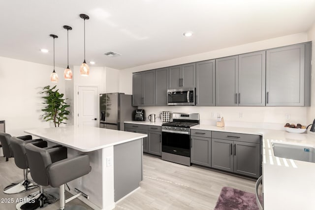 kitchen with gray cabinetry, hanging light fixtures, a kitchen island, and appliances with stainless steel finishes