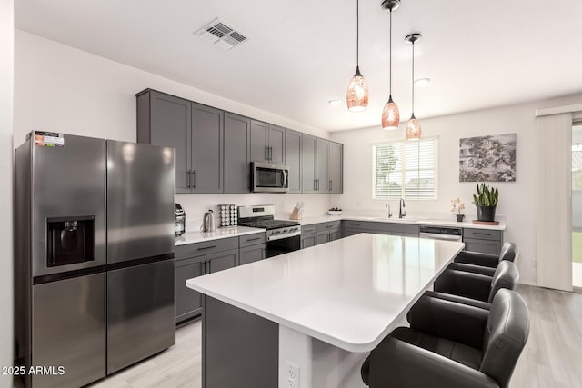 kitchen with gray cabinets, stainless steel appliances, a kitchen breakfast bar, a center island, and decorative light fixtures