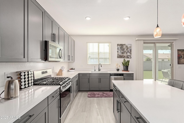 kitchen with gray cabinets, appliances with stainless steel finishes, sink, hanging light fixtures, and light hardwood / wood-style flooring