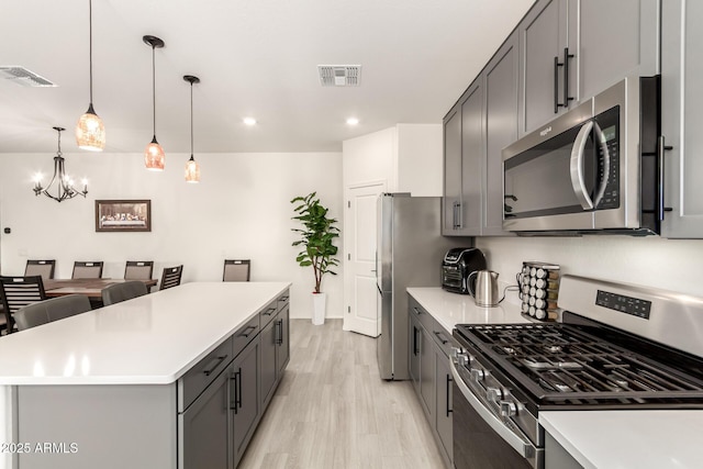 kitchen featuring decorative light fixtures, gray cabinetry, a center island, stainless steel appliances, and light wood-type flooring