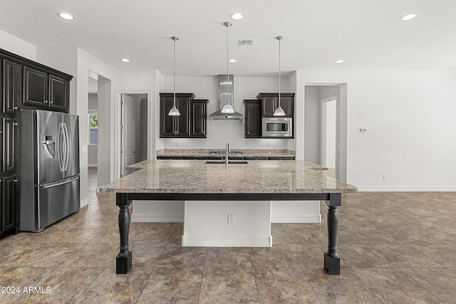 kitchen featuring a large island with sink, hanging light fixtures, stainless steel appliances, and wall chimney exhaust hood