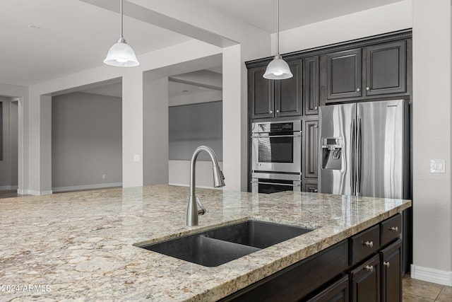 kitchen with appliances with stainless steel finishes, light stone countertops, light tile patterned flooring, sink, and decorative light fixtures