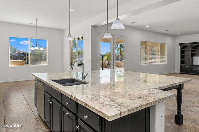 kitchen with hanging light fixtures, a center island with sink, light stone counters, dishwasher, and sink